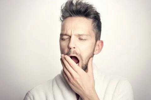 Portrait d'un homme blanc qui est en train de bailler, la main devant la bouche